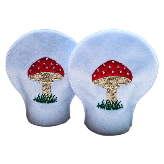 Pair of unlit embroidered toadstool tealight covers made from soft felt, showing red stitched toadstools and grassy details for a cosy woodland inspired display.