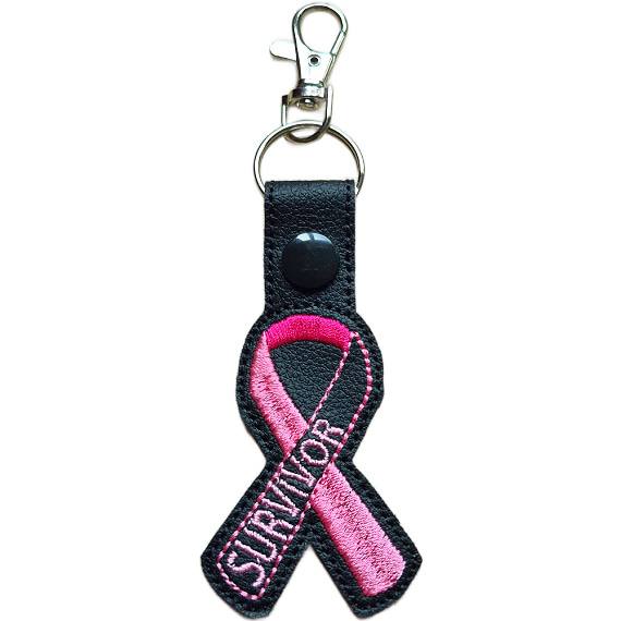 Embroidered Survivor awareness ribbon keyring made from black faux leather, featuring a pink stitched ribbon design with black snap and silver metal hardware.