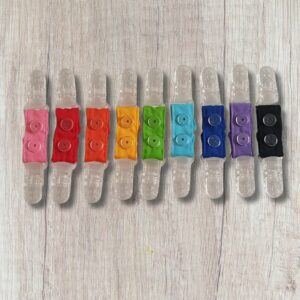 A row of handmade double ended clothing clips in bright colours including pink, red, orange, yellow, green, turquoise, blue, purple and black, with clear plastic clips at each end.