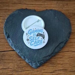 Funny gamer badge design with the phrase 'Gaming is self care' in bold lettering, decorated with small video game controller accents.
