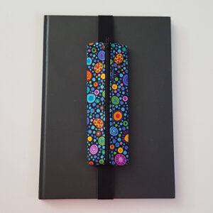 Handmade A4 planner zipper pouch in colourful spot print cotton fabric, shown fitted around a black A4 notebook with a black zip and elastic strap, holding pens and small stationery items.