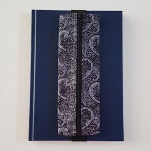 Handmade A5 planner zipper pouch in black and white paisley print cotton fabric, shown fitted around a navy A5 notebook with a black zip and elastic strap, holding pens and small stationery items.