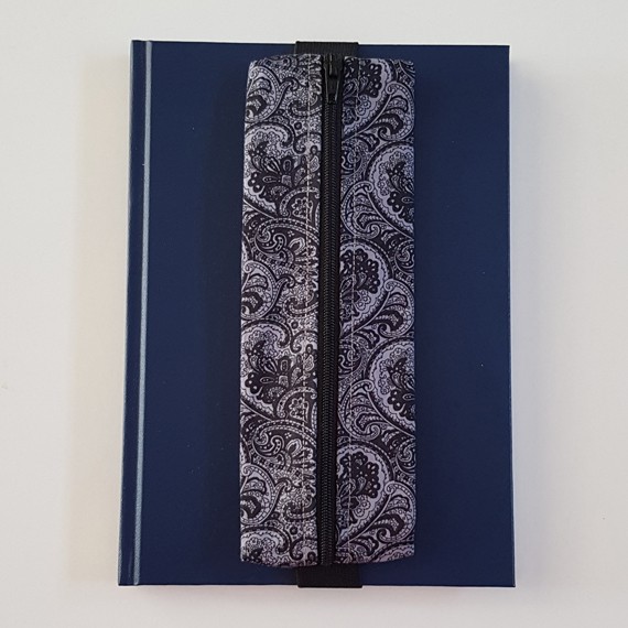 Handmade A5 planner zipper pouch in black and white paisley print cotton fabric, shown fitted around a navy A5 notebook with a black zip and elastic strap, holding pens and small stationery items.