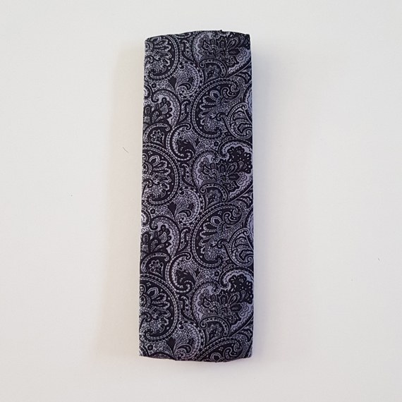 Handmade A5 planner zipper pouch in black and white paisley print cotton fabric, shown fitted around a navy A5 notebook with a black zip and elastic strap, holding pens and small stationery items.