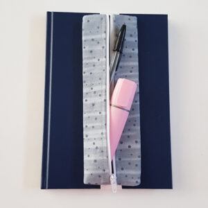Handmade A5 planner zipper pouch in grey spot print cotton fabric, shown fitted around a navy A5 notebook with a white zip and elastic strap, holding pens and small stationery items.