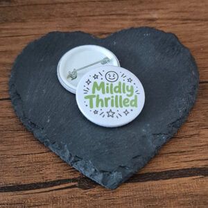 Mildly Thrilled funny mood badge with playful green lettering, star accents and a small smiley face, available as a badge, magnet or keyring.