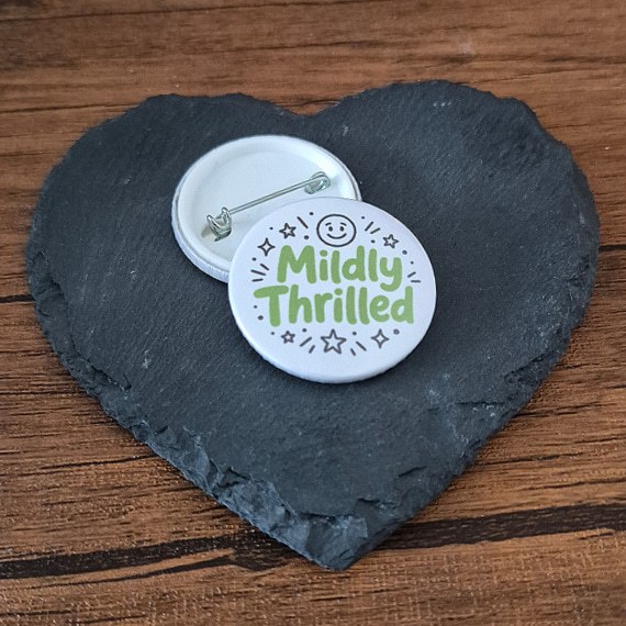 Mildly Thrilled funny mood badge with playful green lettering, star accents and a small smiley face, available as a badge, magnet or keyring.