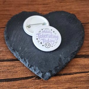 Funny mood badge design with the phrase 'Mildly tolerating today' in playful lettering, decorated with small star accents and a fed up face detail.