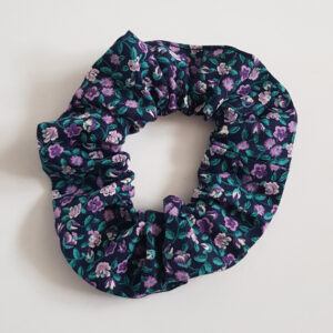 Purple floral cotton scrunchie with green leaves on a dark background.