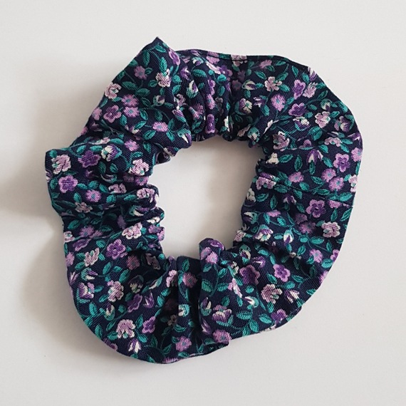 Purple floral cotton scrunchie with green leaves on a dark background.