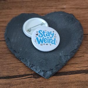 Funny weird badge design with the phrase 'Stay weird' in playful lettering, decorated with small heart, star and doodle accents.