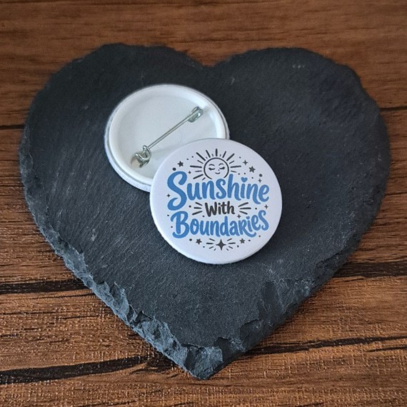 Sunshine With Boundaries positive self care badge with playful blue lettering, a cute sunshine accent and small sparkle details, available as a badge, magnet or keyring.