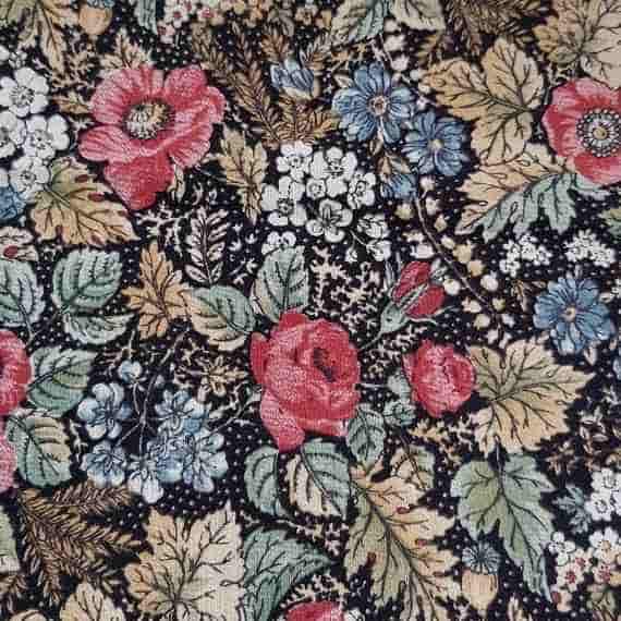 Vintage floral fabric pattern with red roses, blue flowers and pale green leaves on a black background.