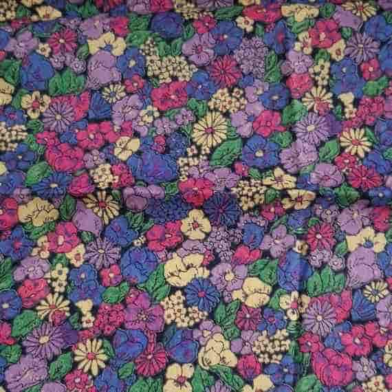 Colourful floral fabric with purple, pink, blue and cream flowers, green leaves and a busy garden print.