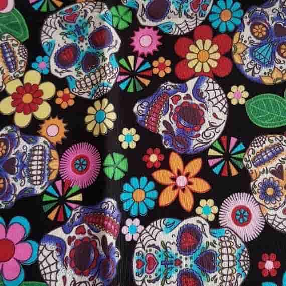 Day of the Dead sugar skull fabric with colourful flowers, hearts and decorative skulls on a black background.