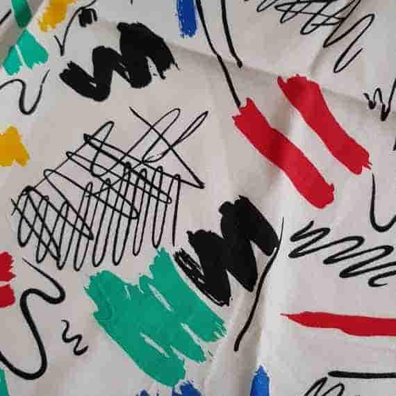 Modern abstract fabric with colourful paint-style marks, black sketch lines and bold red, blue, yellow and teal details on cream.