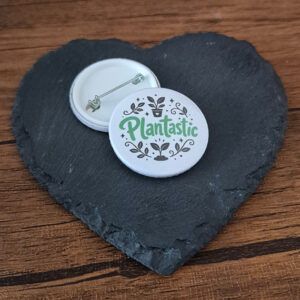 Plantastic funny plant badge with playful green lettering and botanical leaf accents, available as a badge, magnet or keyring.