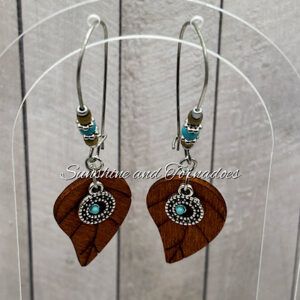 Handmade wooden leaf earrings with tiny 3mm turquoise howlite beads, antique silver accents and hypoallergenic stainless steel ear wires, displayed on a clear jewellery stand against a rustic wooden background.