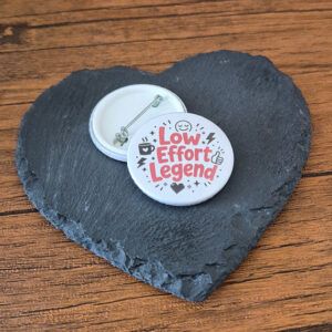 Low Effort Legend funny mood badge with playful red lettering, small sparkle details and cheerful little accents, available as a badge, magnet or keyring.