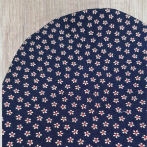 Handmade blue daisy stoma bag cover with tiny white flowers, red centres and dark navy fabric, shown close up on a wooden background.