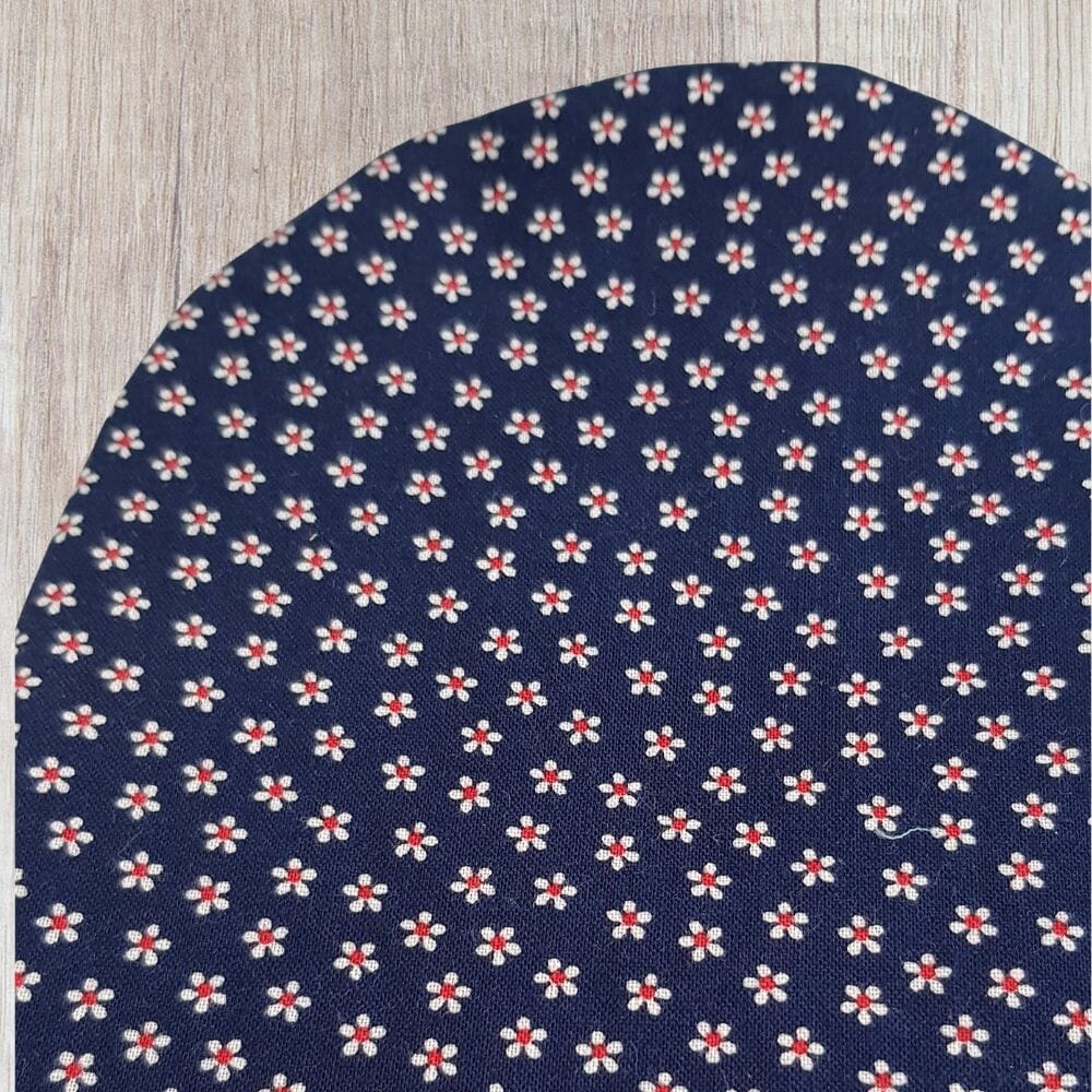Handmade blue daisy stoma bag cover with tiny white flowers, red centres and dark navy fabric, shown close up on a wooden background.