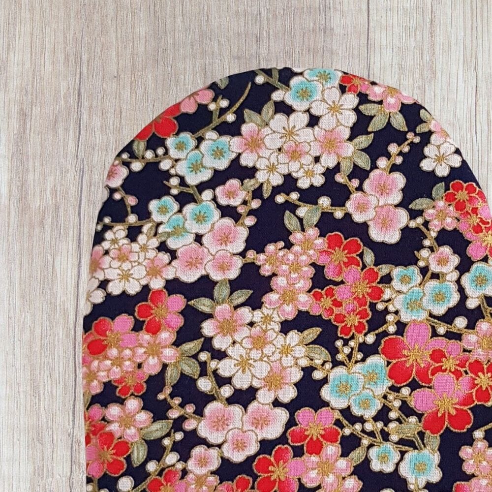 Handmade cherry blossom stoma bag cover with pink, red, cream and blue floral fabric, gold-style branch details and dark navy background.