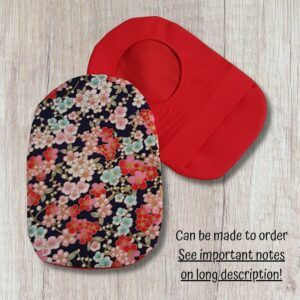 Two handmade stoma bag covers on a wooden background, showing a cherry blossom patterned front cover with pink, red, cream and pale blue flowers, alongside a plain red reverse cover with an opening.