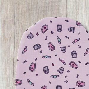 Handmade cute goth stoma bag cover with pastel pink fabric, tiny coffins, gravestones, bats, bones and stars, shown close up on a wooden background.
