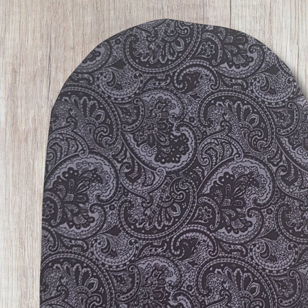 Handmade grey paisley stoma bag cover with black and grey vintage-style swirling fabric, shown close up on a wooden background.