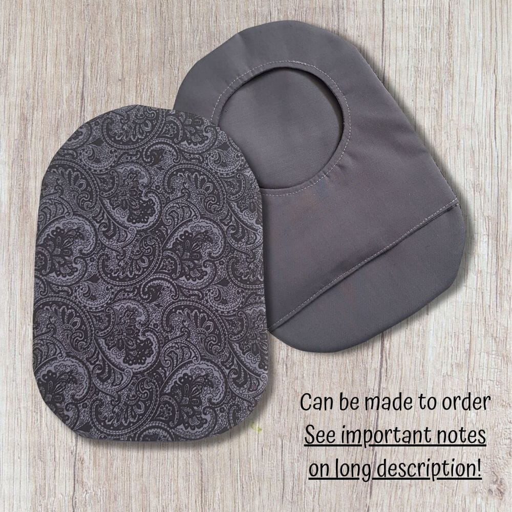 Two handmade stoma bag covers on a wooden background, showing a grey paisley patterned front cover and a plain grey reverse cover with an opening, with text saying can be made to order.