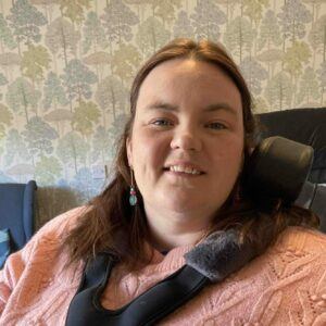 Picture of me. I have brown hair and blue eyes. I am in a wheelchair and am smiling at the camera.
